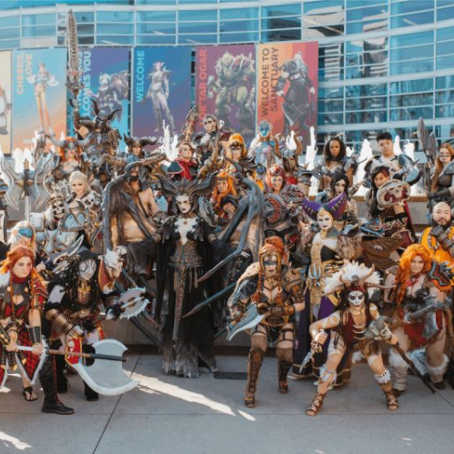 Un numeroso grupo de cosplayers vestidos con detalladas armaduras y trajes de personajes icónicos de sagas de Blizzard como Diablo, World of Warcraft y Overwatch posan reunidos frente al edificio principal del Anaheim Convention Center.
