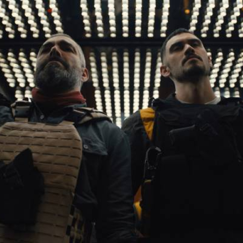 Dos personajes con equipo táctico se encuentran dentro de un elevador iluminado por paneles LED en el techo, creando un ambiente tenso y estilizado.