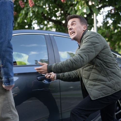 Dos personas discuten junto a un automóvil estacionado en una calle arbolada, en una escena que evoca tensión cotidiana y humor situacional.