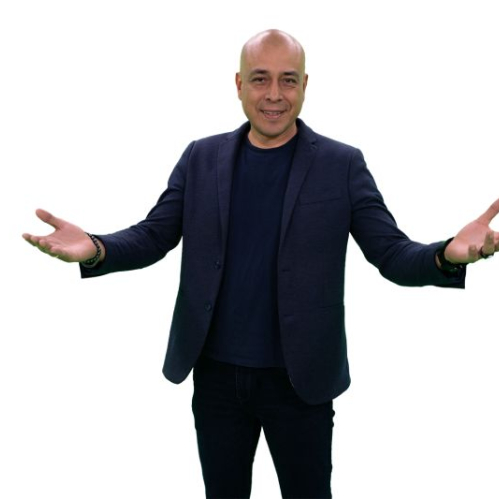 Retrato promocional de estudio del periodista Yohanan Díaz Vargas sobre un fondo blanco uniforme. Se observa al investigador vestido con blazer azul marino, camiseta oscura y pantalones negros, sonriendo hacia la cámara mientras extiende los brazos con las palmas abiertas hacia arriba.