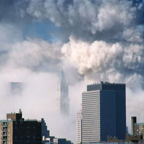 Vista panorámica de la zona financiera de Nueva York donde se observan densas columnas de humo blanco y gris saliendo del complejo del World Trade Center, con la silueta de una de las torres en el fondo rodeada de bruma y edificios del bajo Manhattan.