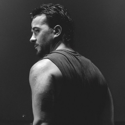 Fotografía en blanco y negro de Luis Fonsi de perfil sobre un fondo oscuro y sumergido parcialmente en agua, bajo el título de la gira en letras azules claras.