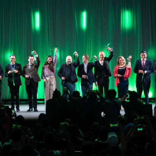 Un grupo de representantes del sector público, educativo y empresarial sostiene listones verdes en un escenario durante una ceremonia inaugural frente a una audiencia.