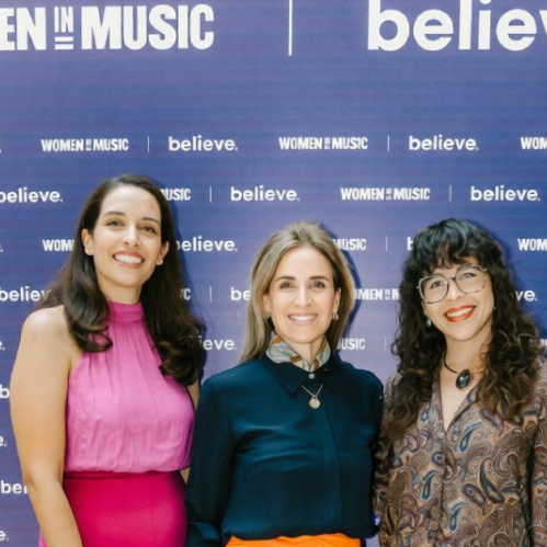 Tres mujeres sonrientes posan en un evento frente a un muro fotográfico azul con los logotipos impresos de Women In Music y Believe. Archivo: NATALIA, ALE, ANDREA.jpg.