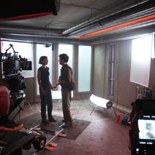 Equipo de filmación capturando una escena entre dos actores en un set con iluminación profesional y cámaras de cine.