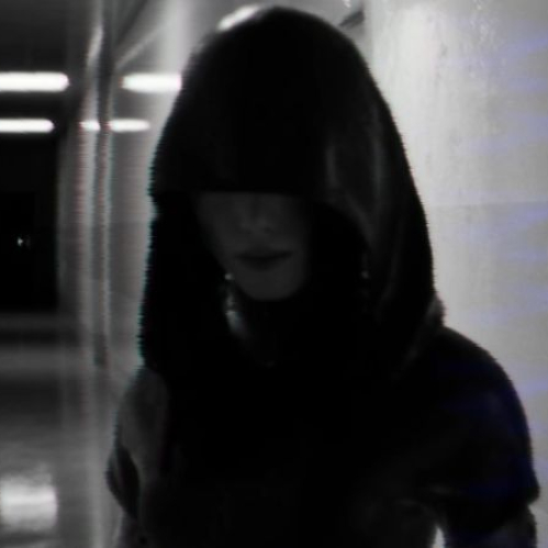 Captura de pantalla de vista en primera persona en BrokenLore: DON’T LIE, mostrando una figura fantasmal o de sombra con capucha avanzando por un pasillo estrecho y sombrío con efecto de distorsión visual.
