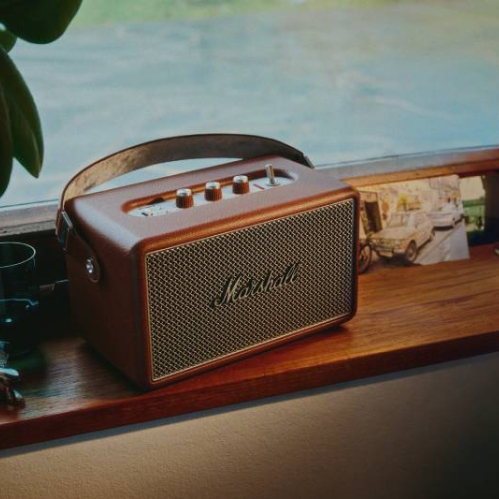 Dispositivo de audio con diseño clásico colocado sobre una repisa de madera, acompañado por objetos decorativos y una iluminación suave que resalta su estética retro.