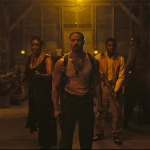 Grupo de intérpretes en un espacio de madera iluminado por lámparas cálidas, con un personaje central al frente y el resto del elenco detrás, evocando un ambiente dramático y de época.