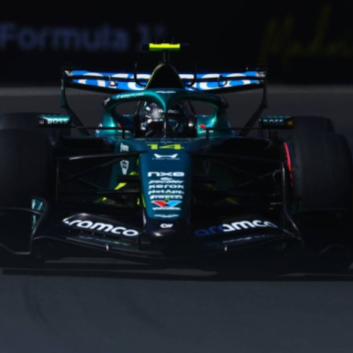Fotografía frontal del monoplaza de Fórmula 1 de la escudería Aston Martin, conducido por el piloto español Fernando Alonso sobre el trazado del Gran Premio de España, destacando la toma aérea verde sobre el casco del conductor y la luz frontal sobre el asfalto.