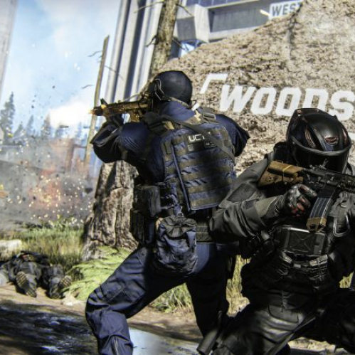 Captura de pantalla en tercera persona del multijugador de Call of Duty: Modern Warfare 4. En el centro, dos soldados con trajes tácticos oscuros y cascos de combate se cubren detrás de un montículo rocoso que lleva la palabra "WOODS" pintada en letras blancas. Uno de los soldados apunta hacia la izquierda con un rifle de asalto dorado, mientras el otro, en primer plano a la derecha, sostiene un rifle negro con ambas manos. A la izquierda, un tercer soldado avanza disparando su arma en medio de una explosión de tierra, y al fondo se aprecian árboles secos y una estructura de concreto gris bajo un cielo parcialmente despejado. El logo del juego aparece en la esquina inferior izquierda.