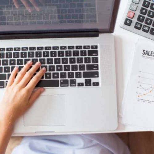 Persona trabajando con una laptop mientras toma notas financieras