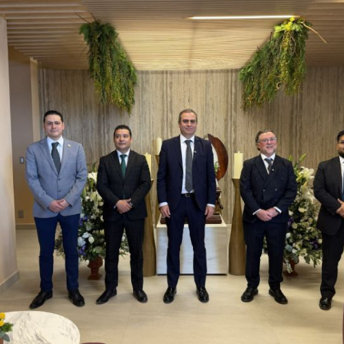 Cinco personas en traje posando en un espacio interior moderno con elementos naturales, arreglos florales y mobiliario contemporáneo.