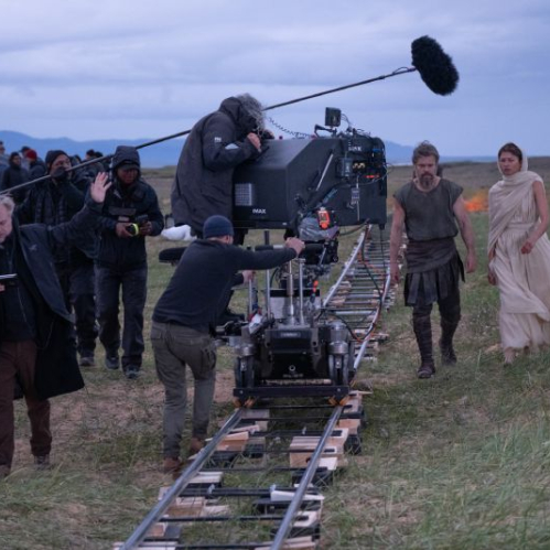 Equipo de filmación trabajando en un set exterior con actores y cámara montada sobre rieles en una producción cinematográfica.