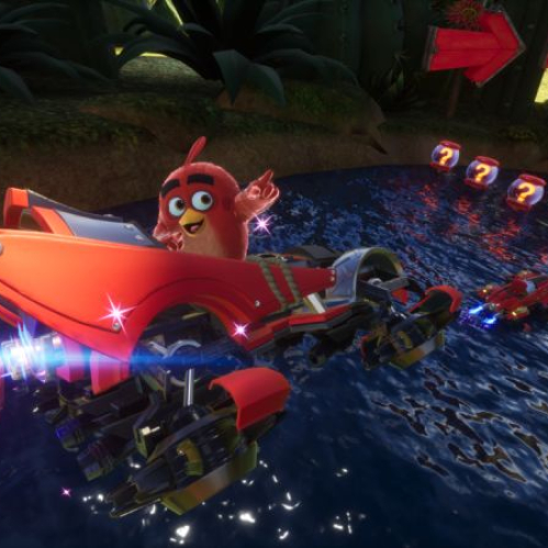 Personaje rojo estilo ave conduciendo un vehículo futurista sobre agua en un entorno colorido con elementos de carrera y cajas flotantes.