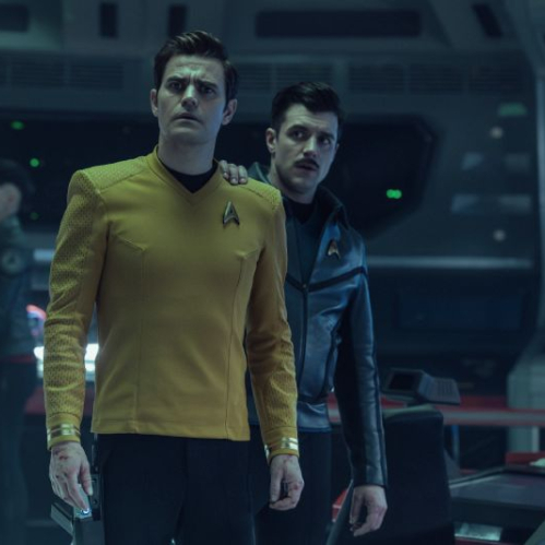 Tres integrantes de una tripulación espacial en una sala de mando futurista, rodeados de paneles y controles tecnológicos.
