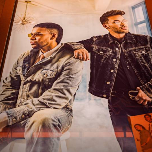 Fotografía promocional con dos artistas posando en un entorno interior moderno, vestidos con prendas de mezclilla y acompañados por una imagen secundaria que complementa la estética de la campaña.