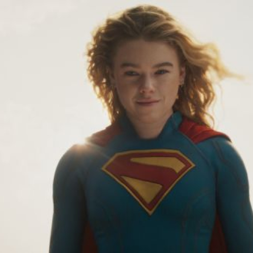 Persona con traje azul y capa roja en pose heroica frente a un cielo iluminado, evocando la estética clásica de una superheroína.