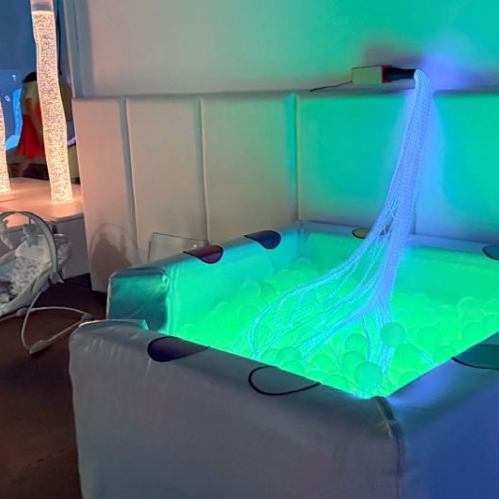 Espacio sensorial con piscina de pelotas iluminada y elementos de estimulación visual.