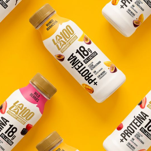 Patrón diagonal de botellas de Yogurt Lala 100 Griego en fondo amarillo, mostrando variedades de sabores como Vainilla, Mango Maracuyá y Wild Berries con la etiqueta que destaca 18g de proteína y 0% lactosa.