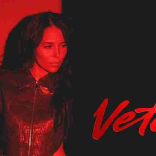 Figura femenina en un entorno oscuro iluminado en tonos rojos, sosteniendo un objeto mientras destaca la palabra “Vete” en tipografía cursiva.