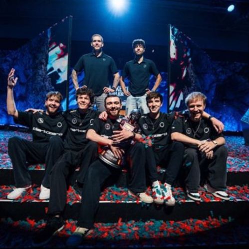 Equipo de esports celebrando en un escenario cubierto de confeti, con un trofeo al centro y pantallas iluminadas al fondo.