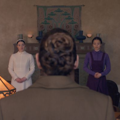 Escena dramática en un salón formal donde dos personajes se enfrentan a una figura sentada, en un ambiente solemne y tenso.