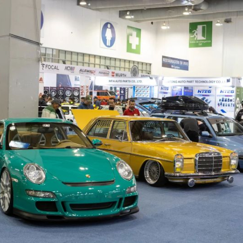 Fotografía del piso de exposición de INA PAACE Automechanika mostrando autos clásicos y deportivos modificados alineados, rodeados por estands de fabricantes de autopartes y asistentes.
