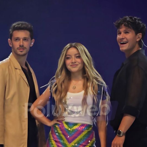 Fotografía de plano medio sobre un fondo azul donde posan sonrientes los tres actores principales de la serie. Del lado izquierdo, Ruggero Pasquarelli luce un saco café claro sobre playera negra; al centro, Karol Sevilla viste una blusa blanca con estampado, chaleco corto azul y una falda multicolor brillante con patrón de zigzag; a la derecha, Michael Ronda viste una camisa negra abotonada y reloj de pulsera.