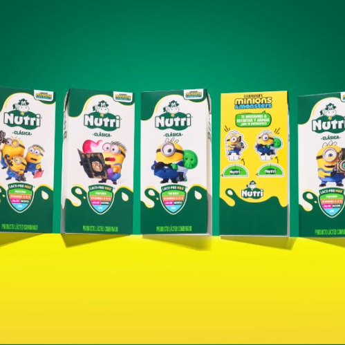 Fotografía de estudio que exhibe cinco empaques en formato tetra pack de la edición especial Nutri Clásica en colaboración con la película Minions & Monstruos. Cuatro envases presentan fondo blanco con verde y personajes como Minions sosteniendo cámaras o portando disfraces, mientras que el envase central muestra un diseño amarillo interactivo con instrucciones para recortar y armar figuras. La composición descansa sobre una superficie amarilla y un fondo verde.
