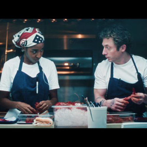 Dos personas trabajando en una cocina profesional, manipulando ingredientes sobre una mesa de acero inoxidable.