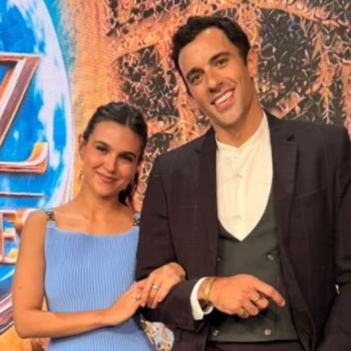Fotografía promocional de los actores Romina Poza y José Pablo Minor sonriendo juntos frente al logotipo oficial de la telenovela 'Luz de mis noches'. Romina Poza, del lado izquierdo, luce un vestido tejible color azul claro con tirantes, mientras sostiene amablemente el brazo de José Pablo Minor, quien viste un traje oscuro con chaleco y camisa blanca sin cuello.