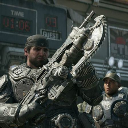 Captura de pantalla de alta resolución de la campaña de "Gears of War: E-Day". En primer plano resalta Marcus Fenix con su característico pañuelo en la cabeza y armadura pesada de la CGO, sosteniendo entre sus manos el prototipo improvisado del rifle Lancer equipado con una motosierra. Al fondo se observa a un soldado con gorra militar y estructuras metálicas de un estadio urbano con marcadores electrónicos bajo la luz del día.