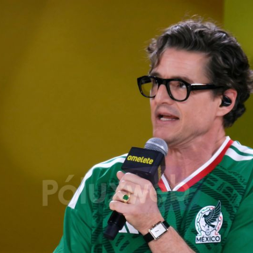 Persona con playera de la Selección Mexicana sosteniendo un micrófono con el logo de Omelete, sobre un fondo amarillo, en un ambiente de entrevista o panel.