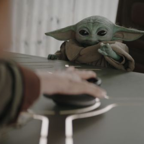 Grogu observa atentamente mientras interactúa con un dispositivo en una escena de la película “Star Wars: The Mandalorian and Grogu”.