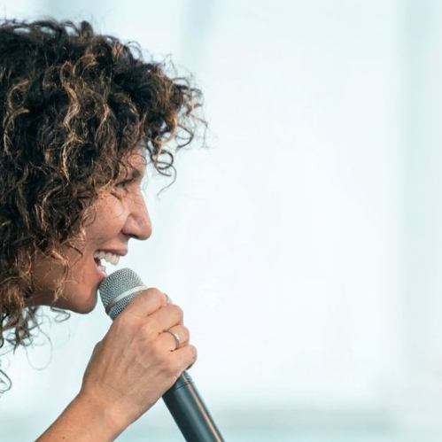 Persona sosteniendo un micrófono en un entorno iluminado suavemente, enfocada en la expresión vocal.