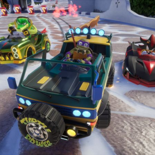 Captura de pantalla de una carrera en Sonic Racing: CrossWorlds. En el centro aparece Donatello conduciendo la camioneta Pizzafire Van (verde y amarilla con una rebanada de pizza en el techo y la leyenda Turtle Power en la llanta de refacción). Flanqueándolo en la pista se encuentran Vector the Crocodile a la izquierda en un auto dorado y verde, y Shadow the Hedgehog a la derecha en un bólido negro y rojo.