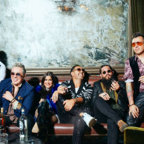 Integrantes de la banda Matute posando juntos en un sillón de piel dentro de un salón elegante, luciendo vestimenta de estilo moderno y gafas oscuras frente a una mesa con botellas.