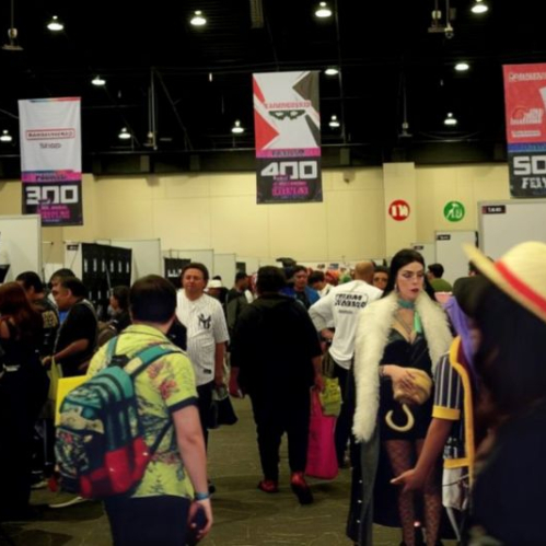 Vista general del piso de exhibición de AniMole 4 en el WTC de la Ciudad de México, mostrando pasillos amplios transitados por asistentes y cosplayers, bajo banners publicitarios con números de pasillos colgando del techo.
