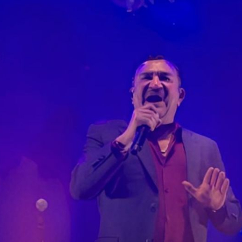 Tony Meléndez interpretando con pasión frente al micrófono en el escenario iluminado con tonos azules durante el concierto de Conjunto Primavera en la Arena CDMX.