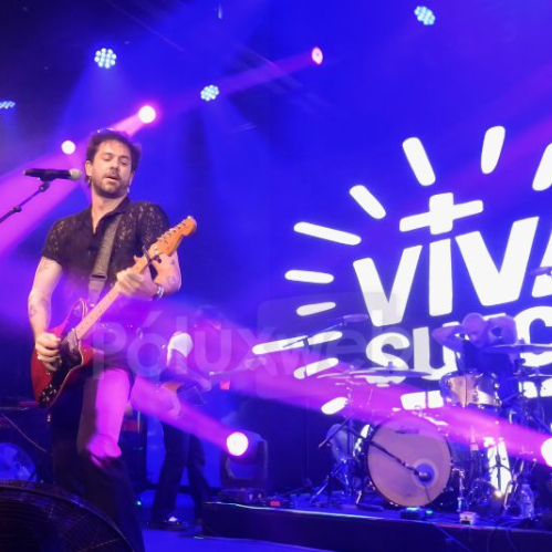 Guitarrista y baterista en escenario iluminado con logo de Viva Suecia al fondo.