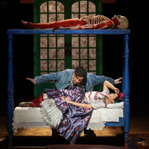 Escena teatral con cama, figuras esqueléticas y estética inspirada en el Mictlán.