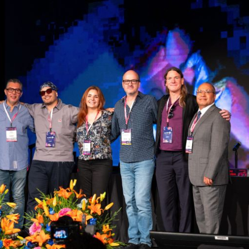 Grupo de especialistas en un escenario con acreditaciones y una pantalla luminosa detrás.