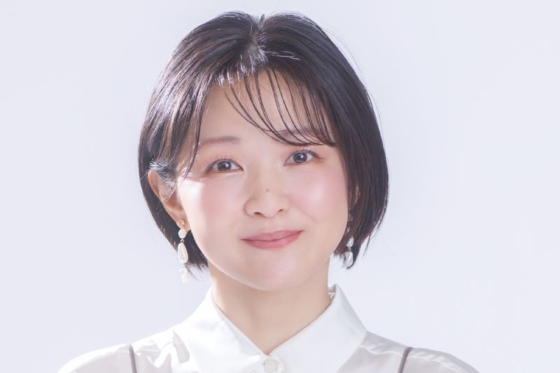 Chiwa Saito, actriz de voz japonesa de Homura Akemi en "Puella Magi Madoka Magica: Walpurgisnacht Rising". Fotografía de estudio de la actriz de voz japonesa Chiwa Saito. Aparece en plano medio, luciendo cabello corto estilo bob de color castaño oscuro con fleco recto. Viste una blusa blanca de cuello cerrado debajo de un top translúcido en tono gris drapeado. Sonríe mirando hacia la cámara con un fondo claro e iluminado.