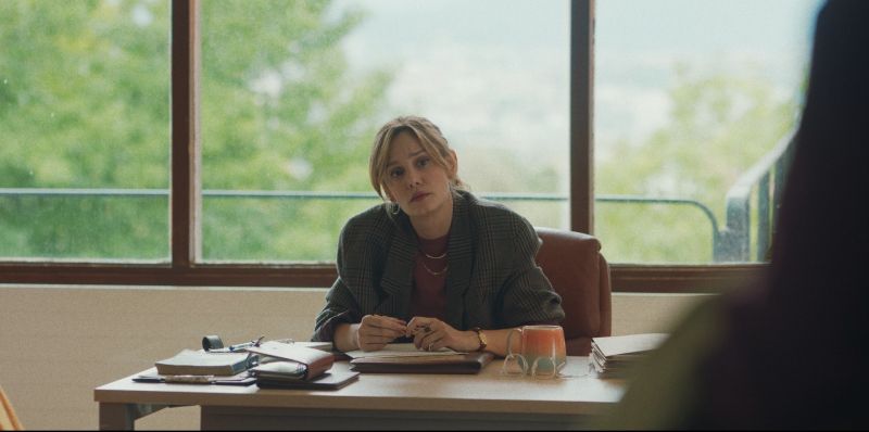 Escena en oficina – Boulevard Persona sentada en un escritorio con documentos y objetos personales, en un ambiente profesional iluminado por luz natural.