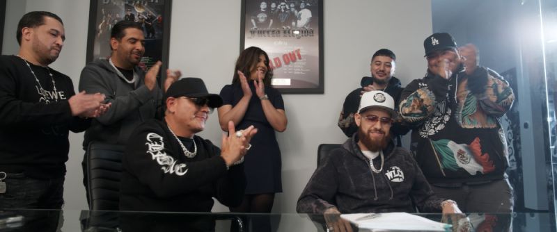 Grupo celebrando la firma de un documento en una oficina con pósters en la pared.
