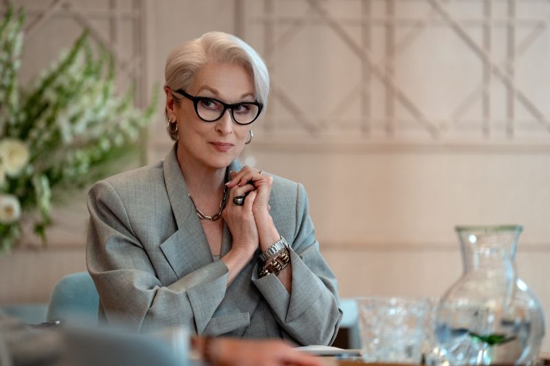 Miranda – El alma de Runway Persona con cabello gris y traje claro sentada en una mesa.