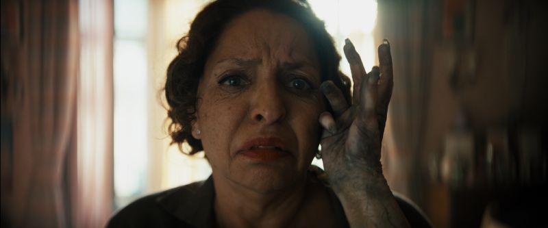 Contacto inquietante – La Posesión de la Momia Una persona con expresión angustiada recibe el toque de una mano oscurecida por suciedad o desgaste. El entorno doméstico contrasta con la tensión del gesto.