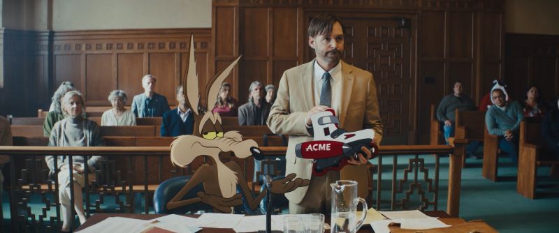 Will Forte sosteniendo un patín defectuoso marca ACME en un tribunal junto al Coyote animado, quien señala resignado ante la sala.