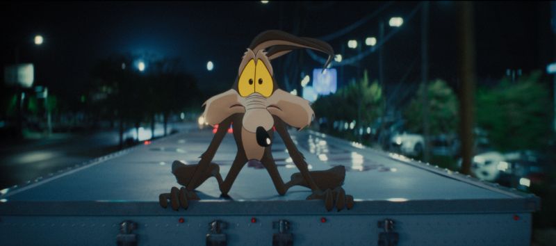 El Coyote en animación 2D luciendo abatido y preocupado mientras viaja sobre el techo de un camión en la carretera durante la noche.