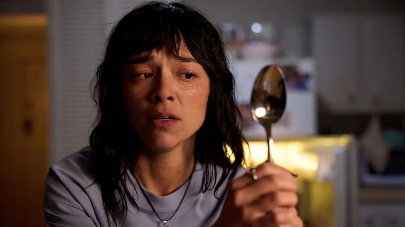 Plano medio de Hanna (Midori Francis) observando fijamente una cuchara metálica en la cocina con rostro angustiado y confundido.
